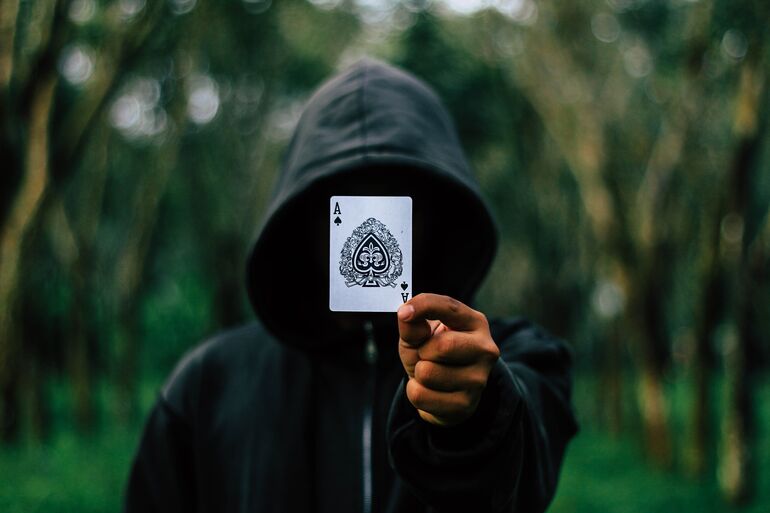 Person with their hood up holding an ace of hearts card up to the camera - Cookiebot