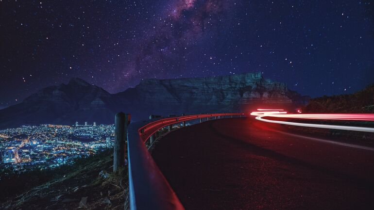 Road with mountain & city in the background at night - Cookiebot