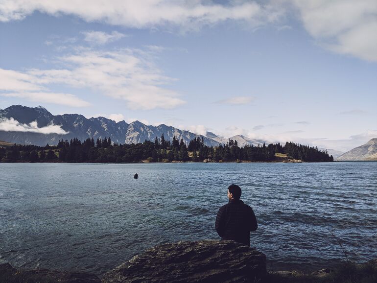 Man looking out over a lake with mountain in the background - Cookiebot